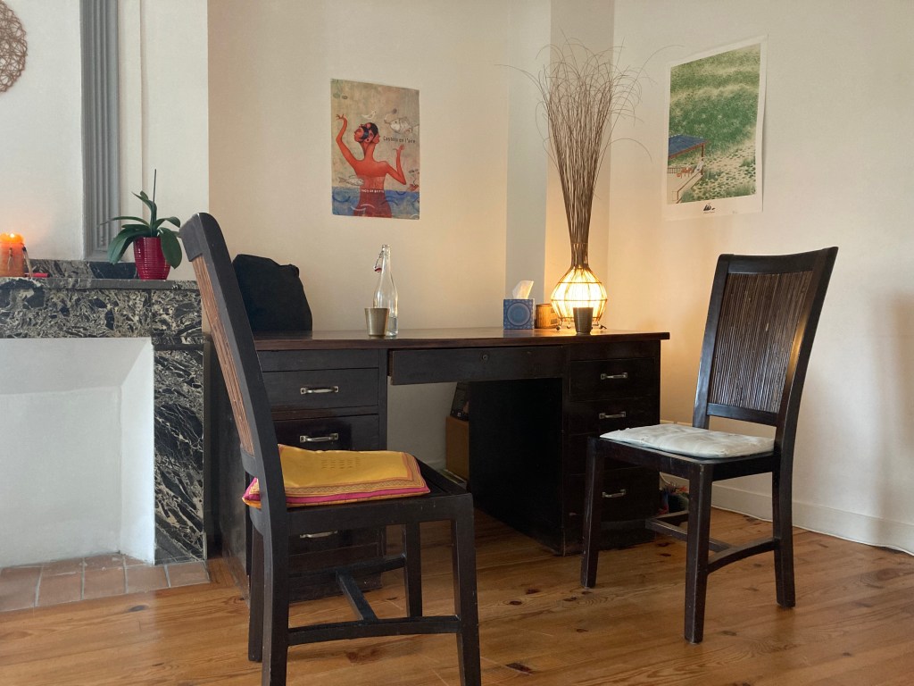 Un bureau en bois avec deux chaises, décoré de plantes et de luminaires, dans un cabinet de consultation.